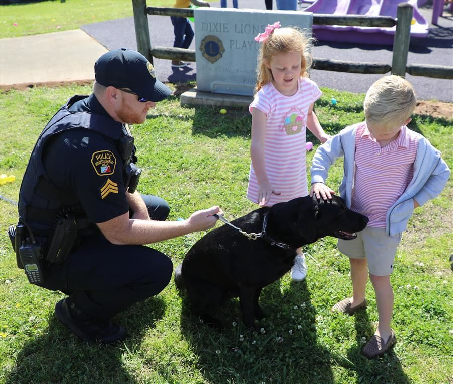 A boy and a girl take a break from hunting Eater Eggs to pet a police k-9. 